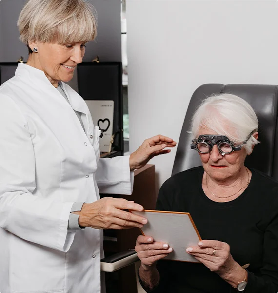 badanie wzroku starszej kobiety z uzyciem okularow probnych i tablicy testowej